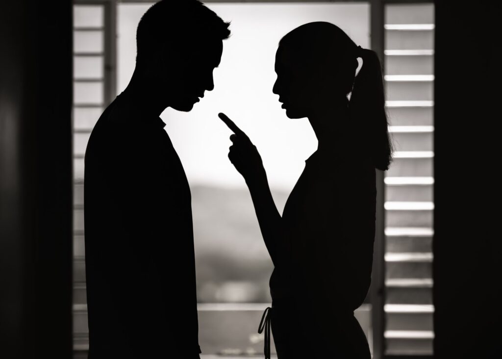 The outline of a man and woman standing face to face. The woman is pointing, with her finger in the man's face.
